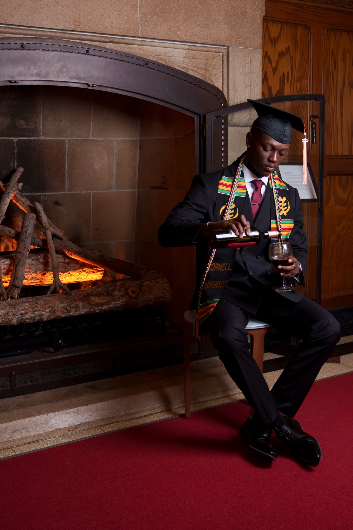 Graduate in formal attire by an ornate fireplace